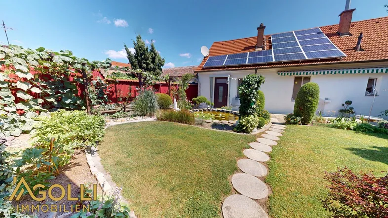 Gepflegter Garten mit Rasenfläche, Teich und Solarpaneelen auf dem Hausdach.