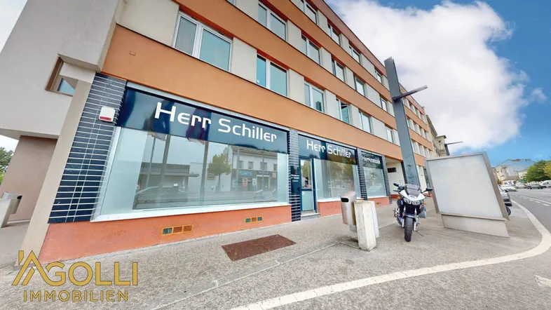 Gebäudeansicht mit Ladenfront 'Herr Schiller' und einer belebten Straße davor.
