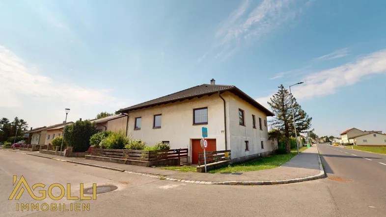 Einfamilienhaus an einer Straßenecke mit umliegender Grünfläche und klarem Himmel.
