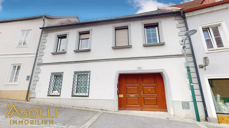 Vorderansicht eines traditionellen Stadthauses mit Holztor und Fenstern zur Straße.