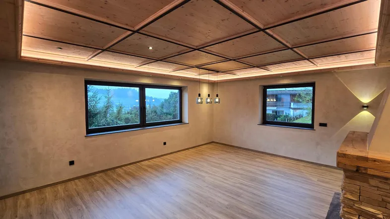 Geräumiger Wohnbereich mit Holzkassettendecke, indirekter Beleuchtung und großen Fenstern.