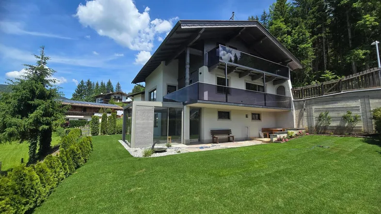 Großzügiger Gartenbereich mit gepflegtem Rasen und moderner Glasveranda am Haus.