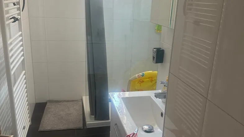 Helles Badezimmer mit Duschkabine, Waschbecken, Spiegelschrank und beheiztem Handtuchhalter.