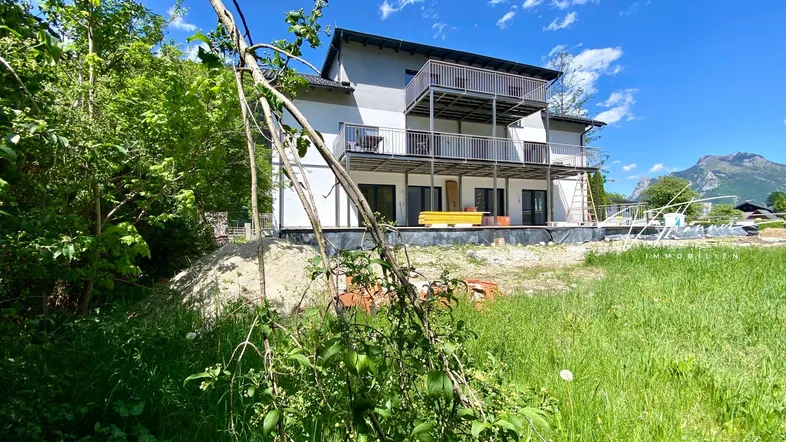 Neubau mit mehreren Balkonen und Blick auf die Berge, umgeben von viel Grün.