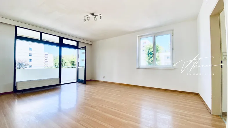 Helles Wohnzimmer mit Parkettboden, weißen Wänden und Zugang zu einem Balkon.