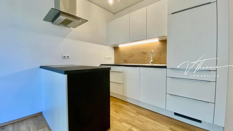 Moderne Küche mit weißen Schränken, Holzakzenten, Dunstabzugshaube und einer kleinen Kücheninsel.