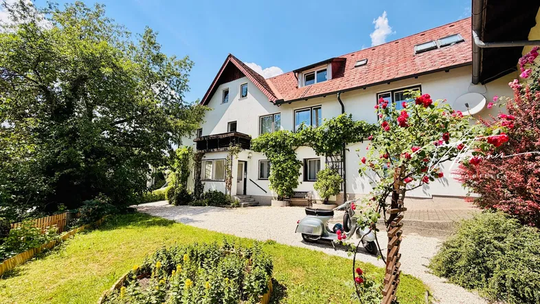 Großzügiger Vorgarten mit gepflegtem Rasen, Blumenbeeten und einer Vespa vor dem Haus.