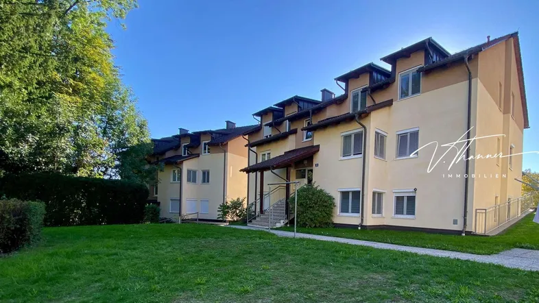Mehrfamilienhaus mit gepflegter Fassade und grüner Umgebung unter blauem Himmel.