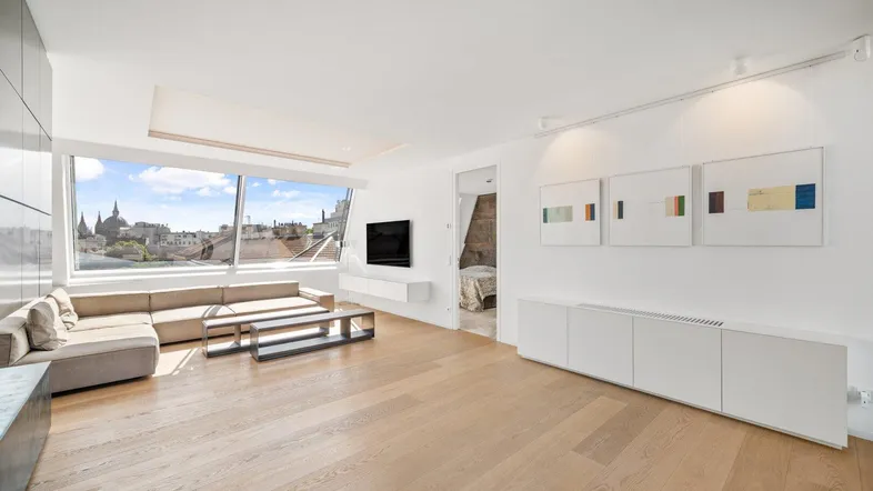 Helles Wohnzimmer mit beigem Sofa, Wandfernseher und Blick auf die Stadt.