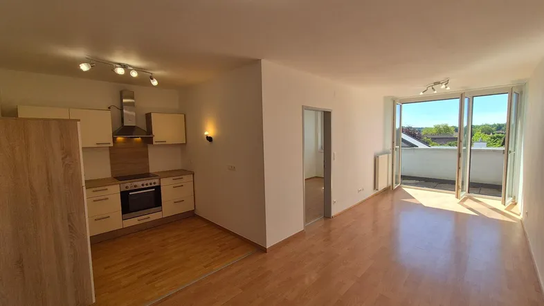 Heller offener Wohnbereich mit integrierter Küche, Laminatboden und Zugang zu einem sonnigen Balkon.