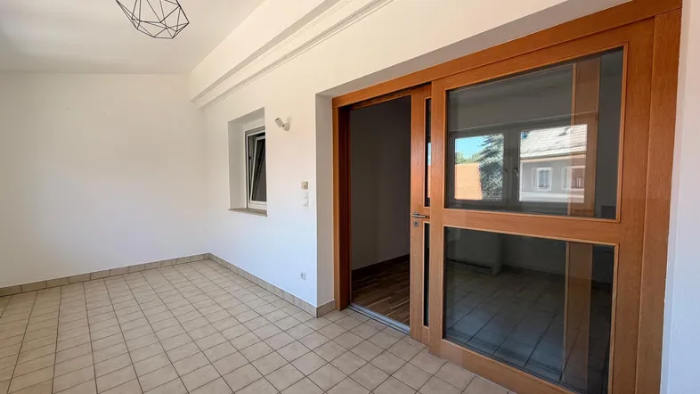 Heller Wohnbereich mit Fliesenboden, großen Schiebetüren und einem modernen Deckenlicht.