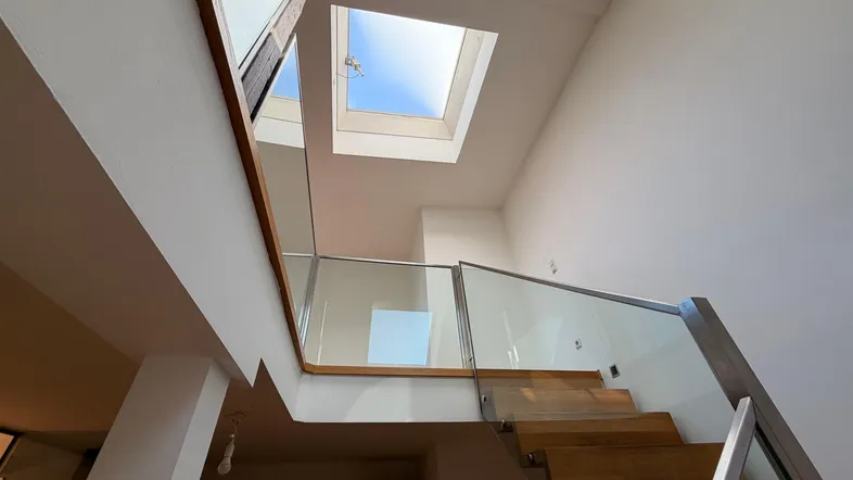 Moderne Holztreppe mit Glasgeländer und Oberlicht, die viel natürliches Licht hereinlässt.
