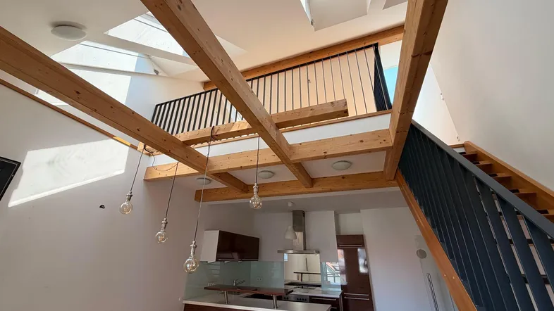 Heller, offener Wohnbereich im Loft-Stil mit sichtbaren Holzbalken, Dachfenstern und einer Galerie.