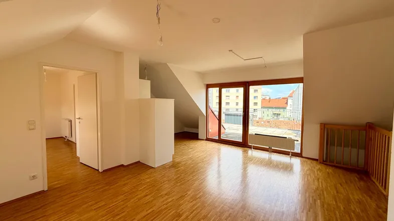 Helles Dachgeschoss-Wohnzimmer mit Parkettboden, Dachschrägen und Zugang zu einer großen Terrasse.