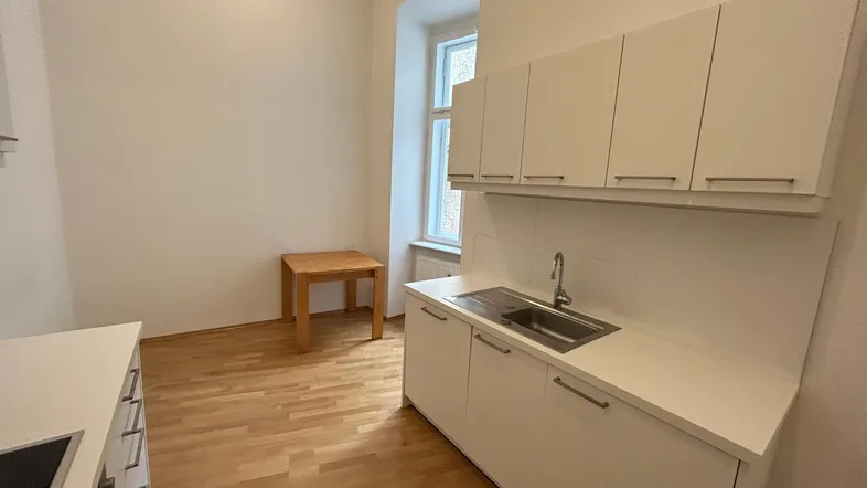 Helle Küche mit weißen Schränken, Spüle und einem kleinen Holztisch, ausgestattet mit Parkettboden.