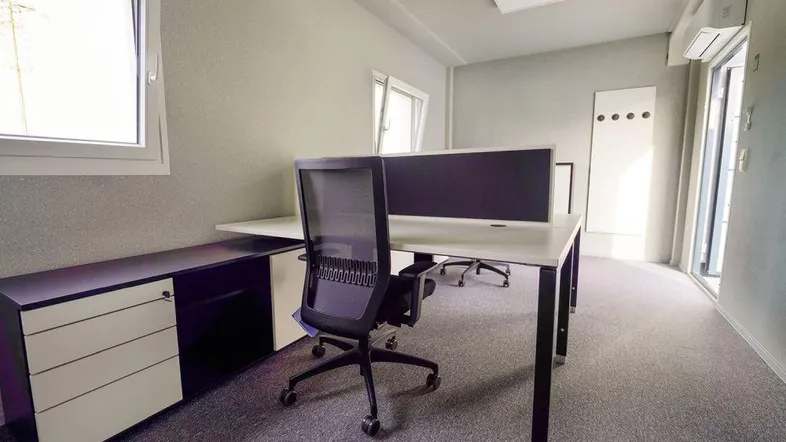 Modernes Büro mit Schreibtischen, Bürostühlen und Fenstern, die viel Tageslicht hereinlassen und eine angenehme Arbeitsatmosphäre schaffen.