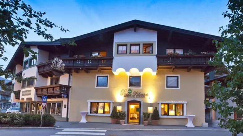 Traditionelles Hotelgebäude im alpinen Stil mit beleuchtetem Eingangsbereich und Holzbalkonen am Abend.