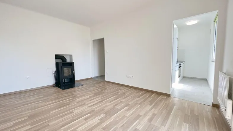 Helles Wohnzimmer mit Holzofen und Parkettboden, mit Zugang zu einem weiteren Raum.