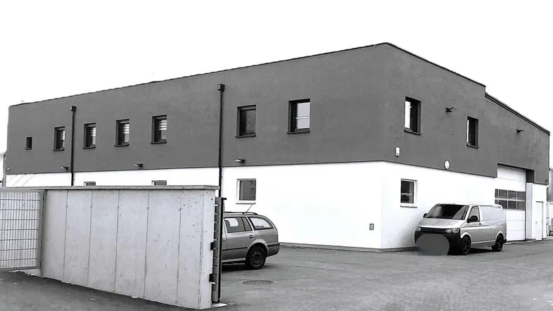 Modernes Geschäftsgebäude mit zweifarbiger Fassade und Parkplätzen davor, unter einem bewölkten Himmel.