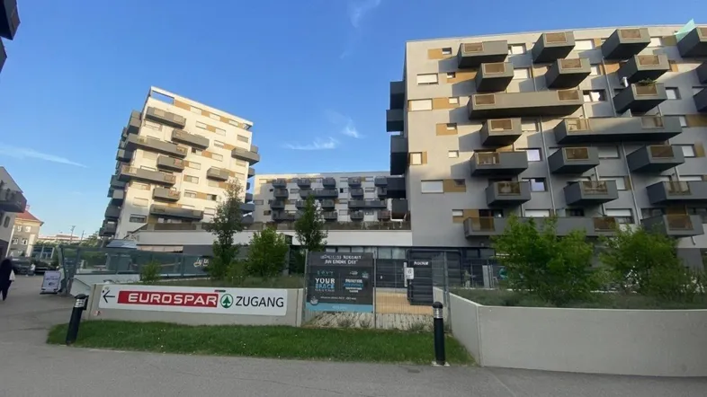 Moderne Wohngebäude mit Balkonen und Geschäften im Erdgeschoss unter blauem Himmel.