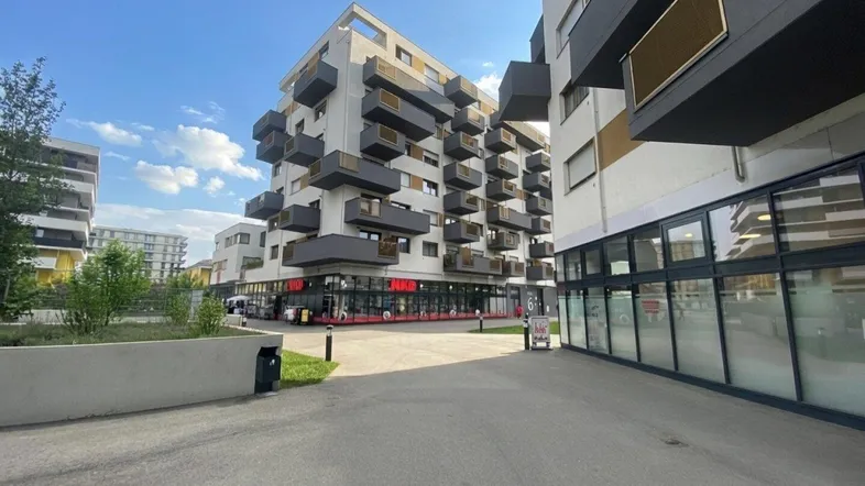 Moderne Wohngebäude mit vielen Balkonen und Geschäften im Erdgeschoss unter blauem Himmel.