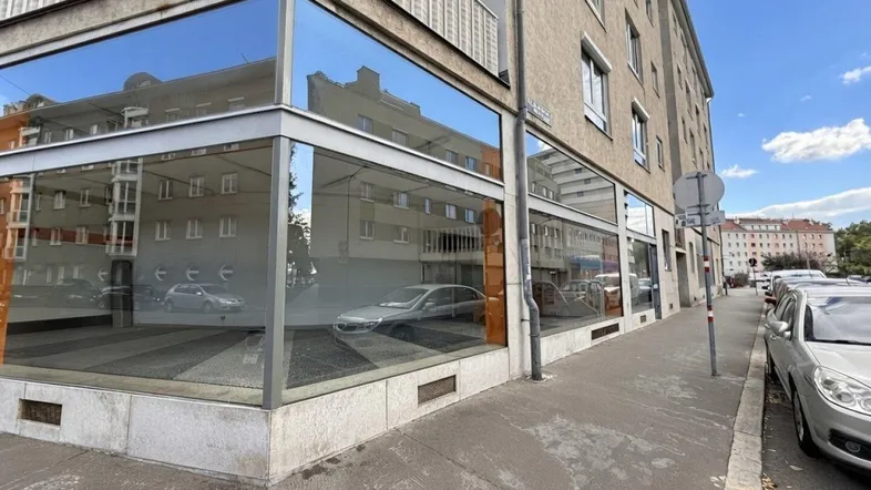 Ansicht des Eckgebäudes mit großen Schaufenstern und Balkonen an einer belebten Straße.