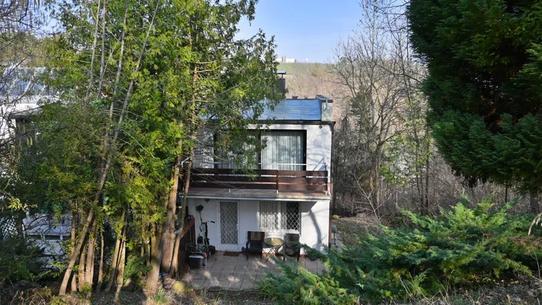 Ansicht des Hauses von außen mit einer möblierten Terrasse im Erdgeschoss und umgebender Natur.