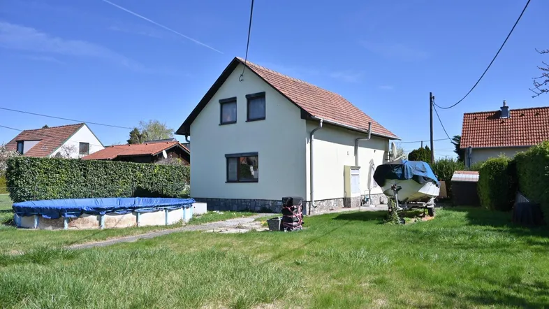 Einfamilienhaus mit großem Garten, Rasenfläche und einem Aufstellpool unter blauem Himmel.
