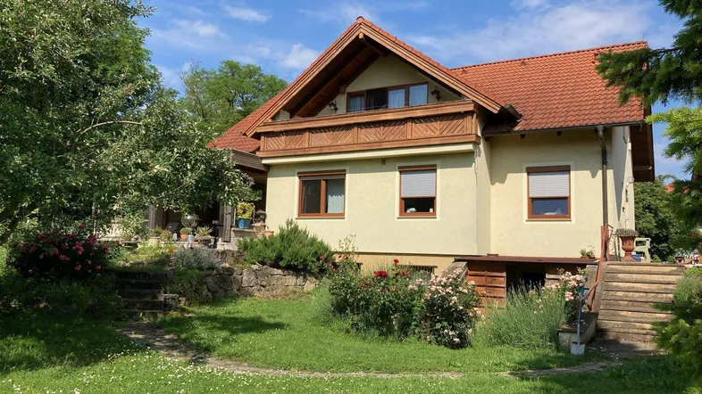 Traditionelles Haus mit Ziegeldach, gelber Fassade und gepflegtem Gartenbereich.