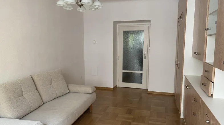Helles Wohnzimmer mit Parkettboden, beiger Couch und integrierten Holzschränken, die viel Stauraum bieten.