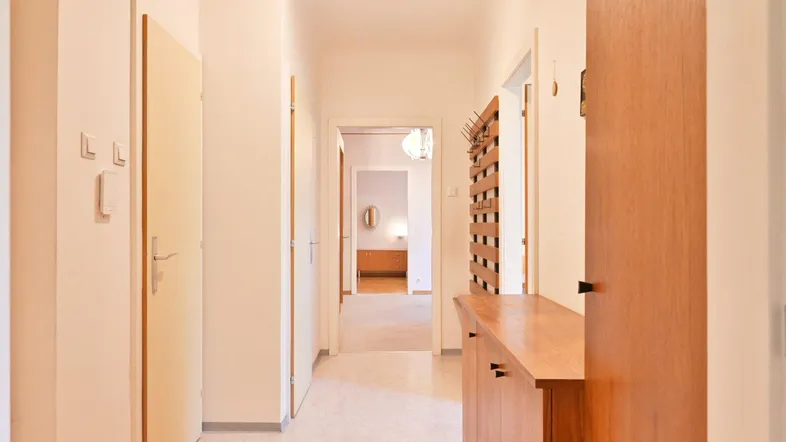 Heller Flur mit Holzmöbeln und Garderobe, der zu weiteren Räumen führt.