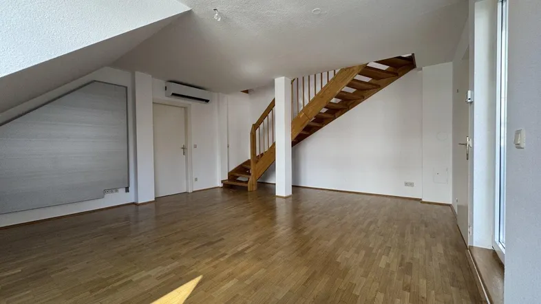 Heller Dachgeschossraum mit Holztreppe, Parkettboden und Klimaanlage, ideal als Wohnbereich.