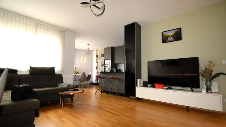 Heller offener Wohn- und Essbereich mit Holzboden, moderner Küche und großem Sofa.