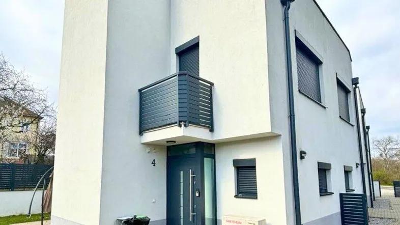 Modernes Reihenhaus mit weißer Fassade, kleinem Balkon und Vorgarten.