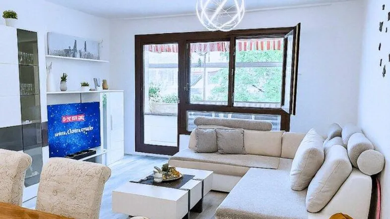 Heller offener Wohn- und Essbereich mit modernem Sofa, Laminatboden und Zugang zum Balkon.