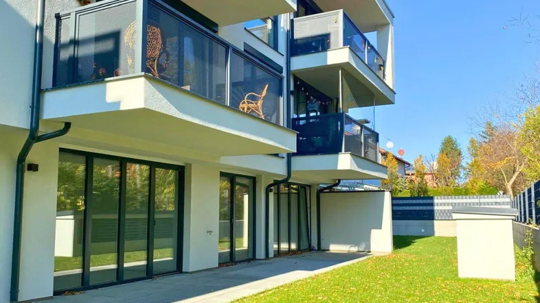Moderne Wohnanlage mit Balkonen, großen Fensterfronten und einer gepflegten Rasenfläche im Erdgeschoss.