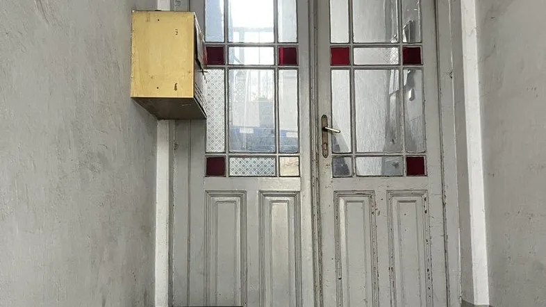 Alte Holztür mit Buntglasfenstern und einem Briefkasten im Eingangsbereich eines Gebäudes.