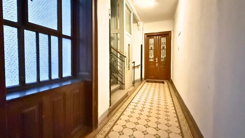 Heller Hausflur mit gemustertem Fliesenboden, Aufzug und einer traditionellen Eingangstür.