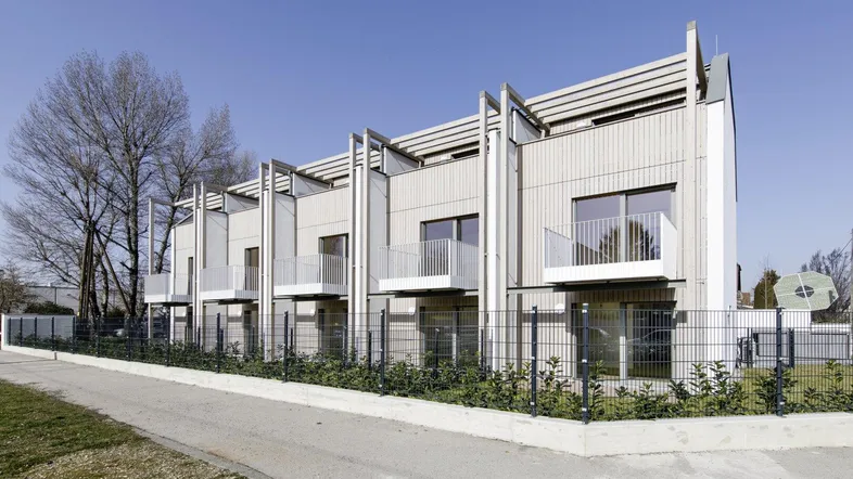 Moderne Reihenhäuser mit Holzfassade und Balkonen unter blauem Himmel.