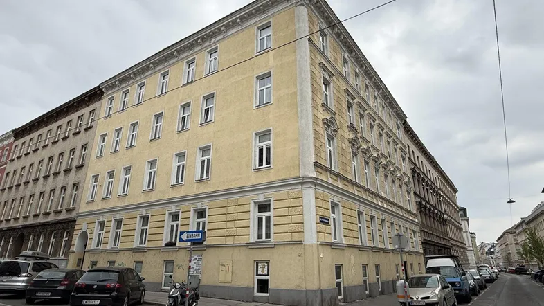 Historisches Eckgebäude mit klassischer Fassade und vielen Fenstern an einer belebten Straße.