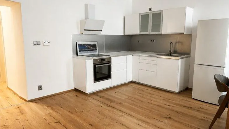 Moderne Küche mit weißen Schränken, integrierten Geräten und hellem Holzfußboden in offenem Wohnbereich.