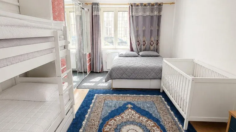 Schlafzimmer mit Etagenbett, Babybett und Doppelbett, ausgestattet mit einem gemusterten Teppich.