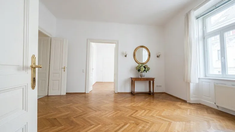 Helles Wohnzimmer mit Fischgrätparkett, hohen Decken und großen Fenstern, das viel Tageslicht bietet.