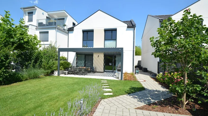 Modernes Einfamilienhaus mit gepflegtem Garten und einer möblierten Terrasse unter einer Pergola.