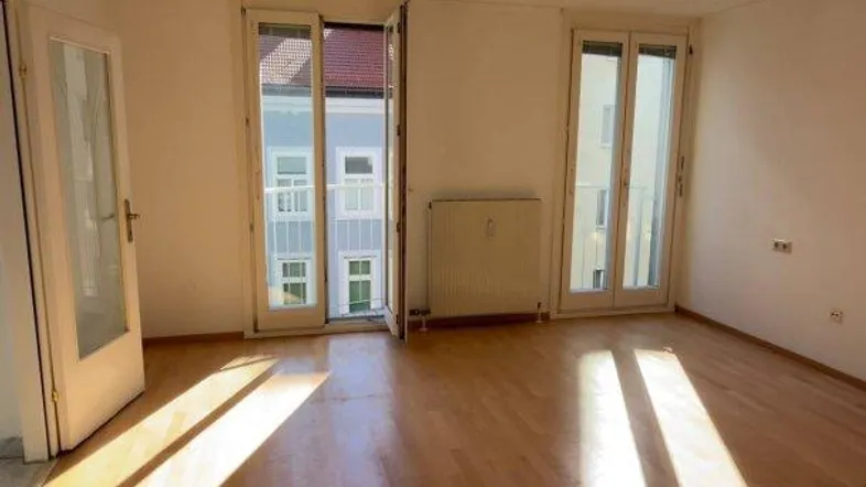 Helles Zimmer mit Holzboden und Zugang zu einem Balkon oder einer Terrasse.