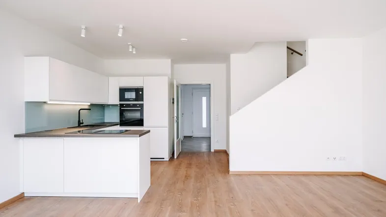 Heller offener Wohnbereich mit integrierter weißer Küche und Laminatboden.