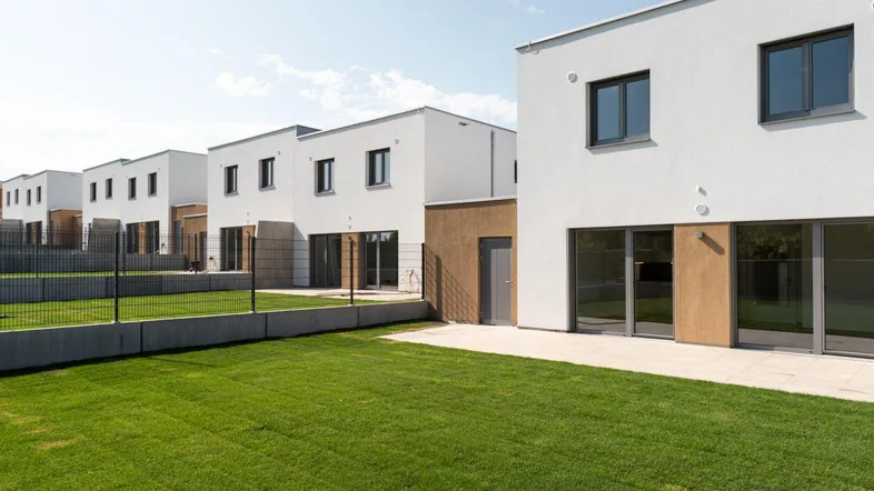 Moderne Reihenhäuser mit weißer Fassade, privaten Gärten und Terrassen in einer neuen Siedlung.