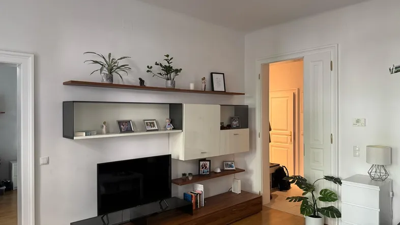 Helles Wohnzimmer mit modernem TV-Möbel, Regalen und Holzboden, das eine gemütliche Atmosphäre schafft.