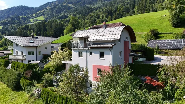 Hausfassade mit mehreren Balkonen und Solaranlage in grüner Berglandschaft.