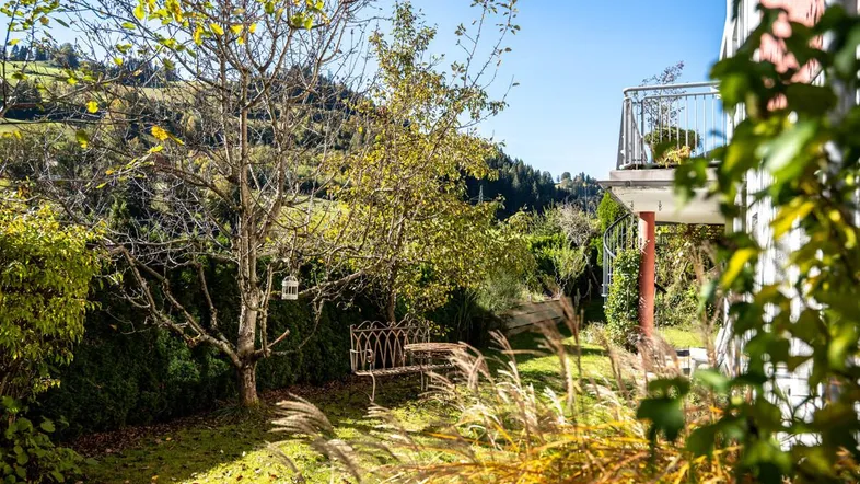 Sonnige Gartenecke mit alter Gartenbank und Blick auf die umliegende Hügellandschaft.
